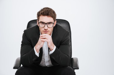 Young pensive business man in eyeglasses sitting on a chair